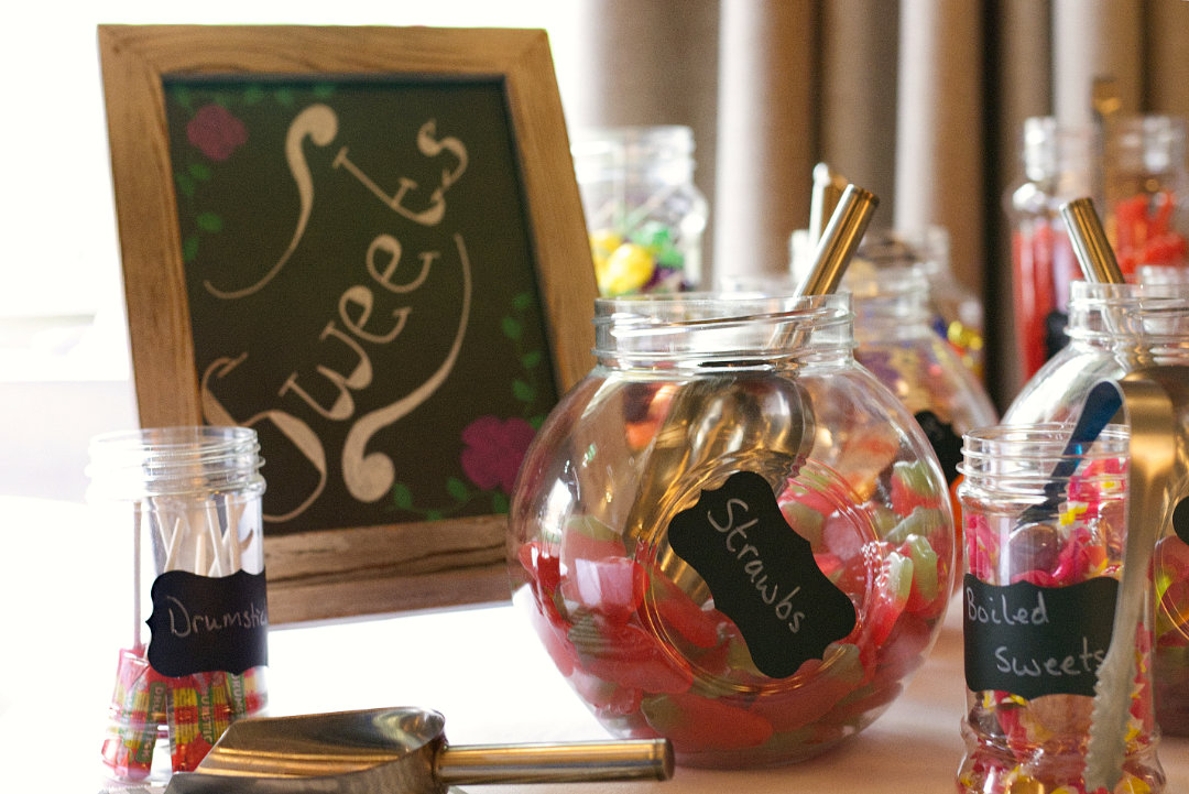 wedding sweetie cart detail photo of jar of various sweets with tongues and spoons sticking out of them and chalk labels on the front