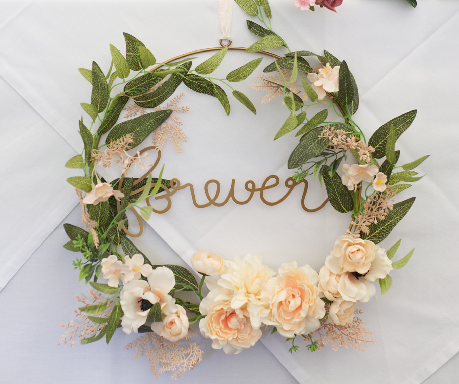 Logo elements ARROWS copyright Nadina Bee wedding decoration: wreath of green leaves and cream roses with the word forever written in gold letters in the centre_for booking alternative wedding photographer Nadina Bee