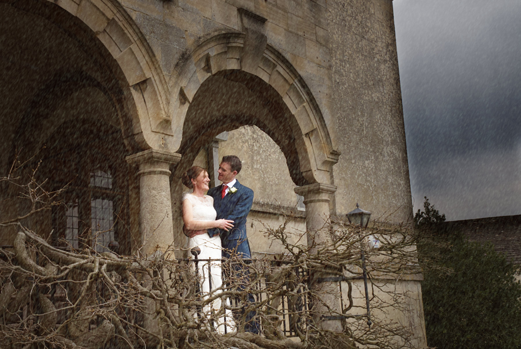 Bad weather on your wedding day - Stunning Rainy day wedding photo of a bride and groom standing on a balcony of a Georgian manor house in the Cotswolds by Gloucestershire wedding photographer Nadina Bee
