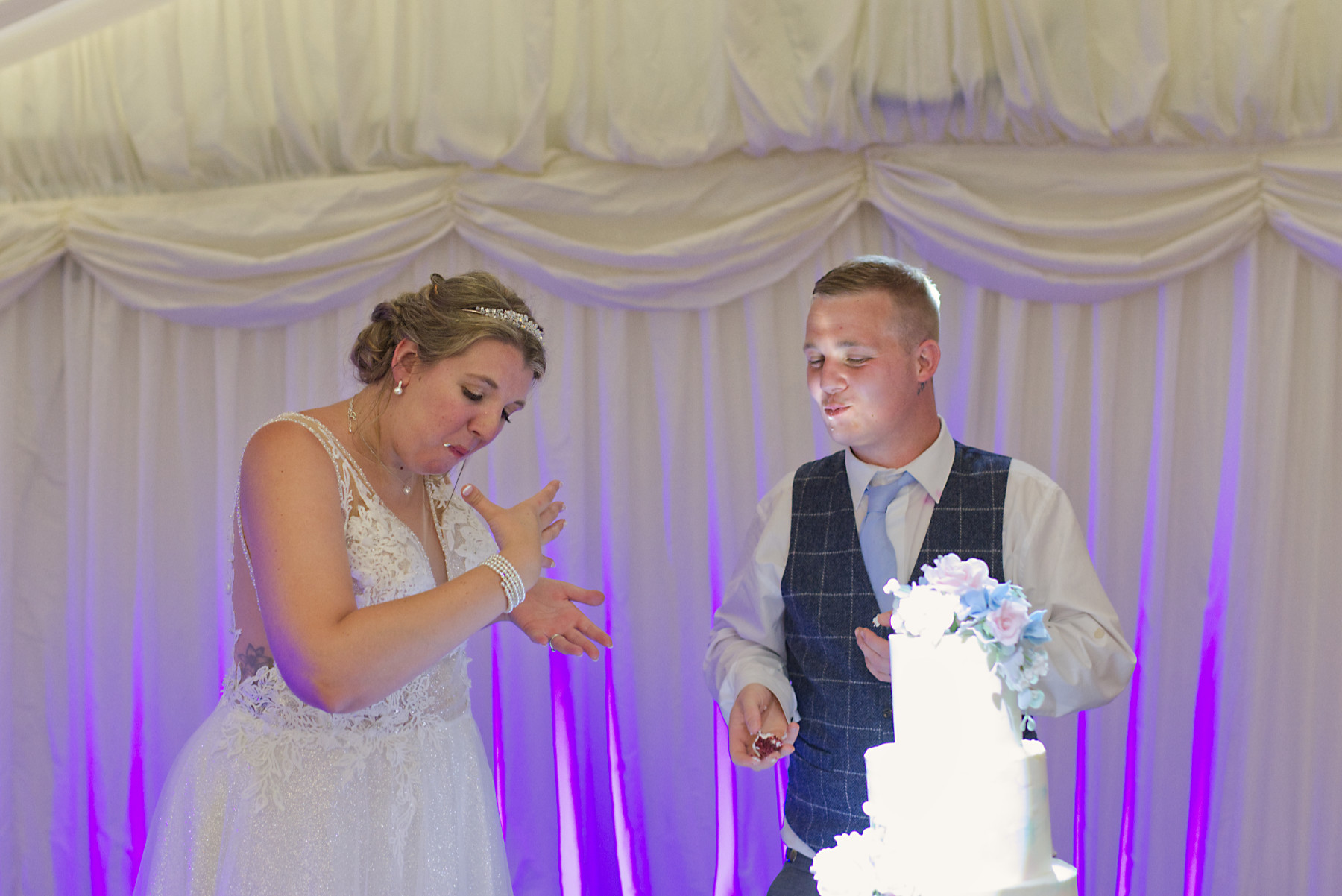 Bride and Groom feeding each other Delicious Wedding Cake with sugar flowers at Mill House Berkshire Wedding Photographer Nadina Bee